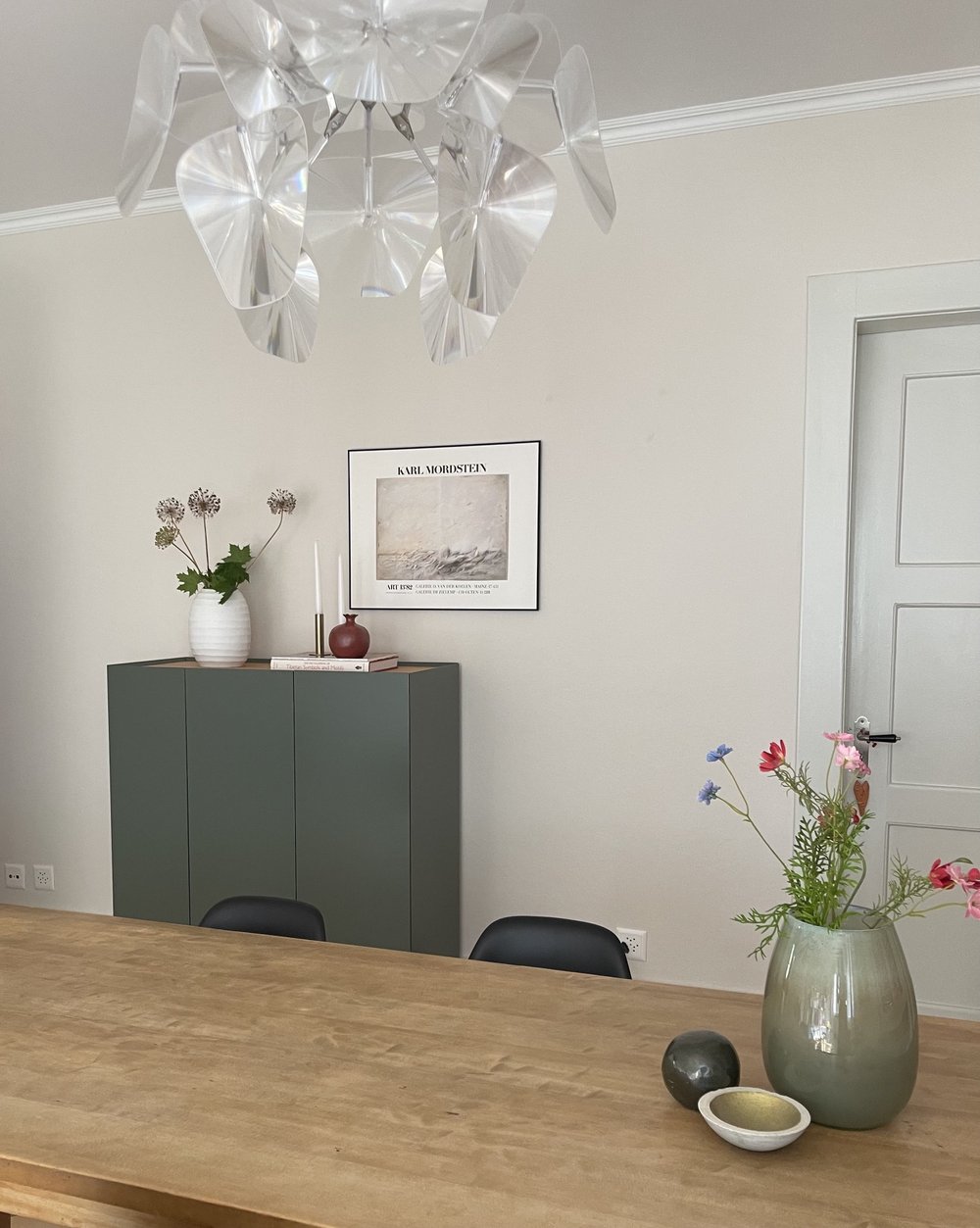 Helle, ruhige Wohnecke mit grünem Sideboard, Kronleuchter und Blumen